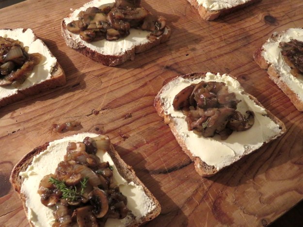 Geschmorte Champignon-Zwiebel-Pfanne mit wilden Kräutern auf geröstetem Brot mit Frischkäse